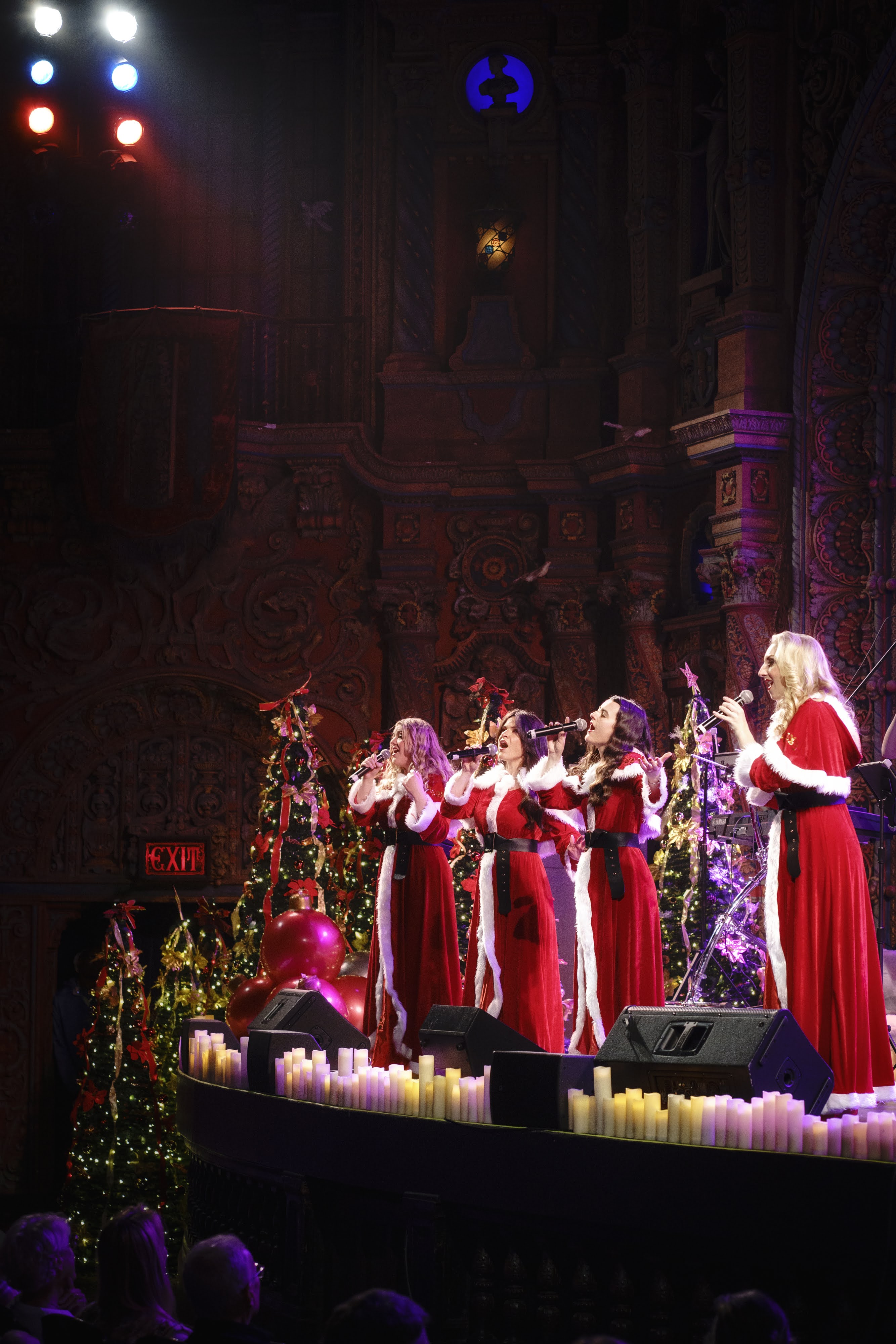 Performers in red dresses on candlelit stage with holiday decorations