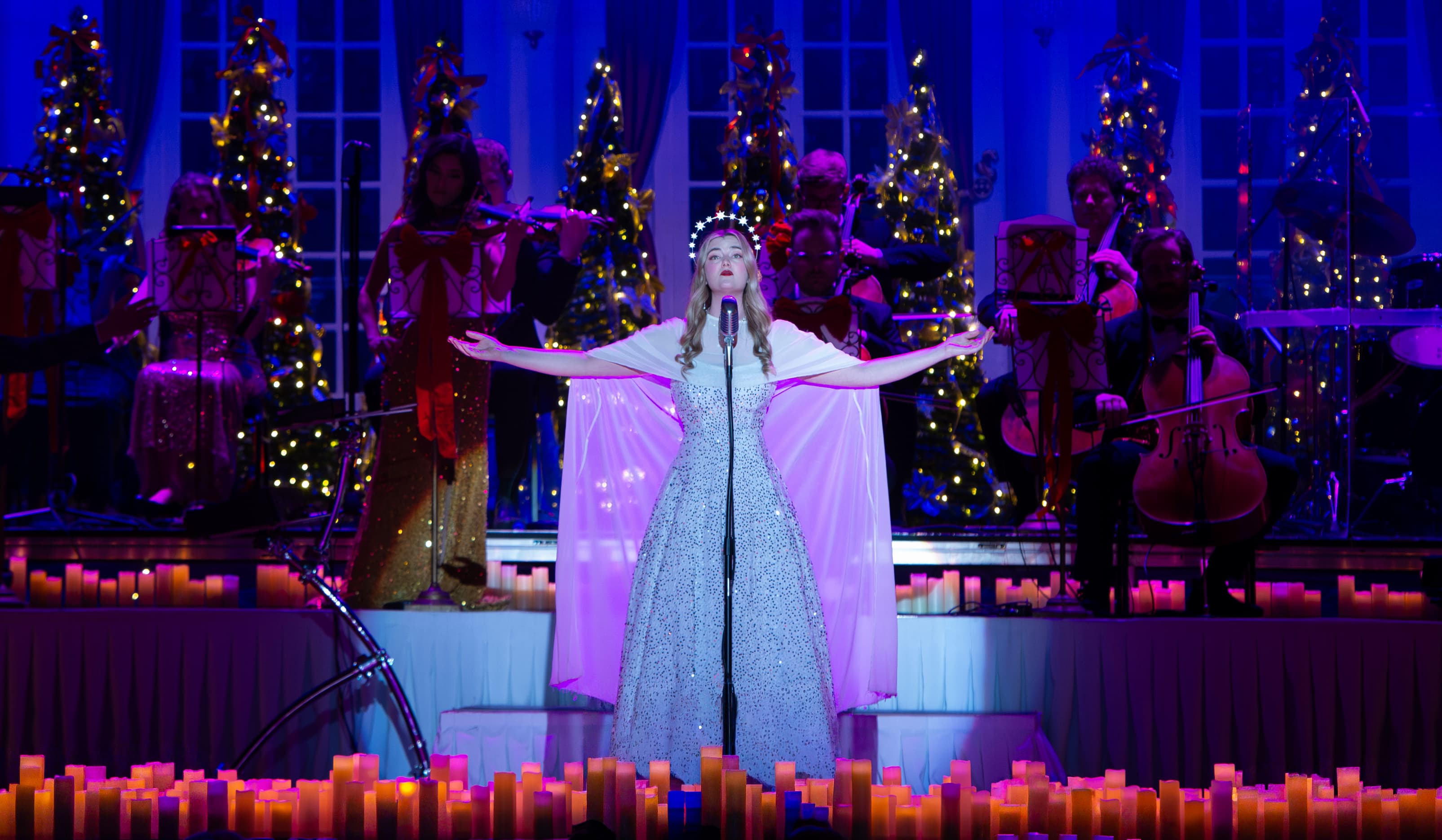 Vocalist in flowing white gown performing Ave Maria on candlelit holiday stage