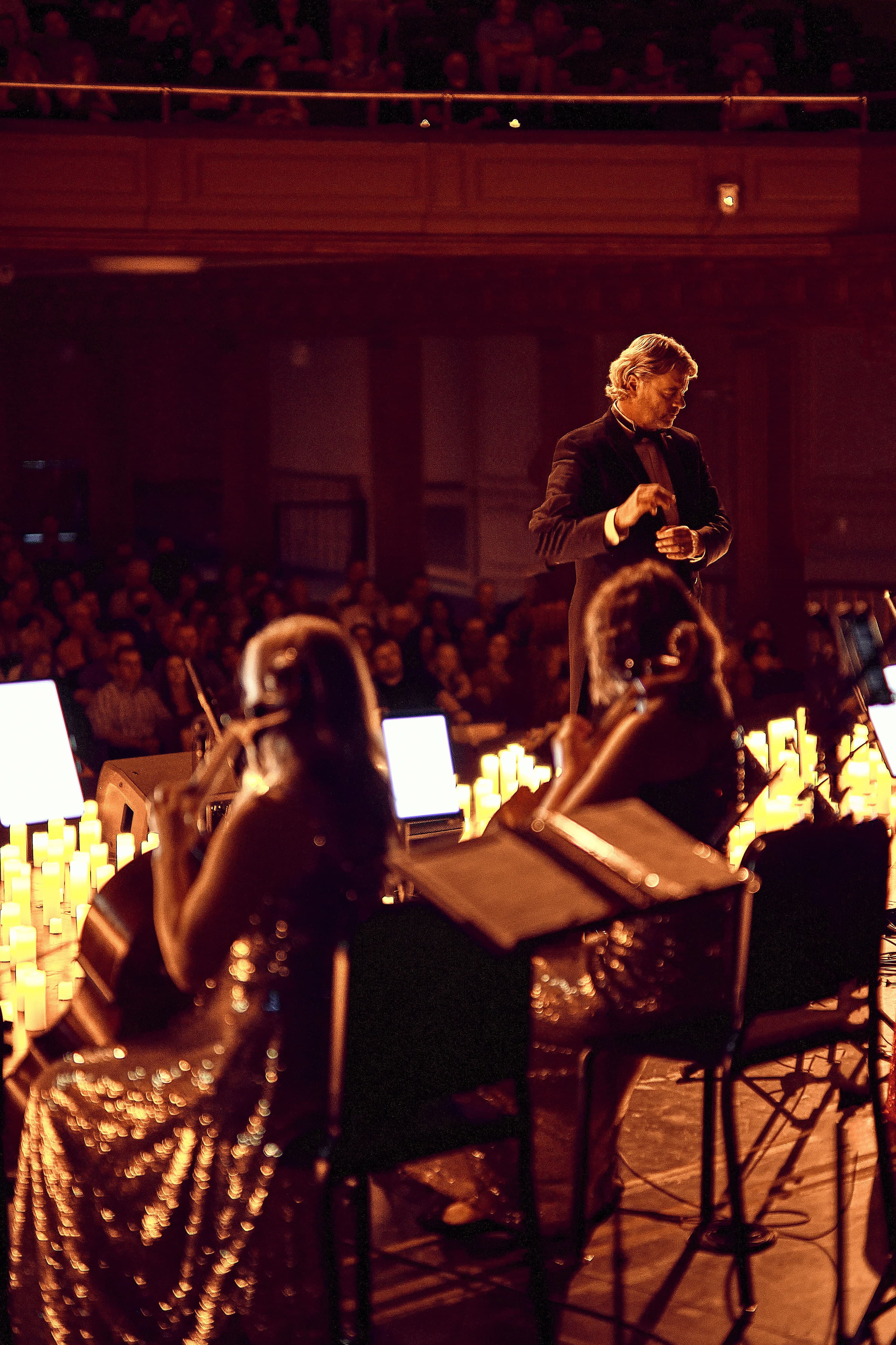 Conductor leading the orchestra surrounded by candlelight